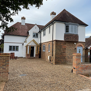 two story house with a brick and white exterior surrounded by gravel driveway and trees